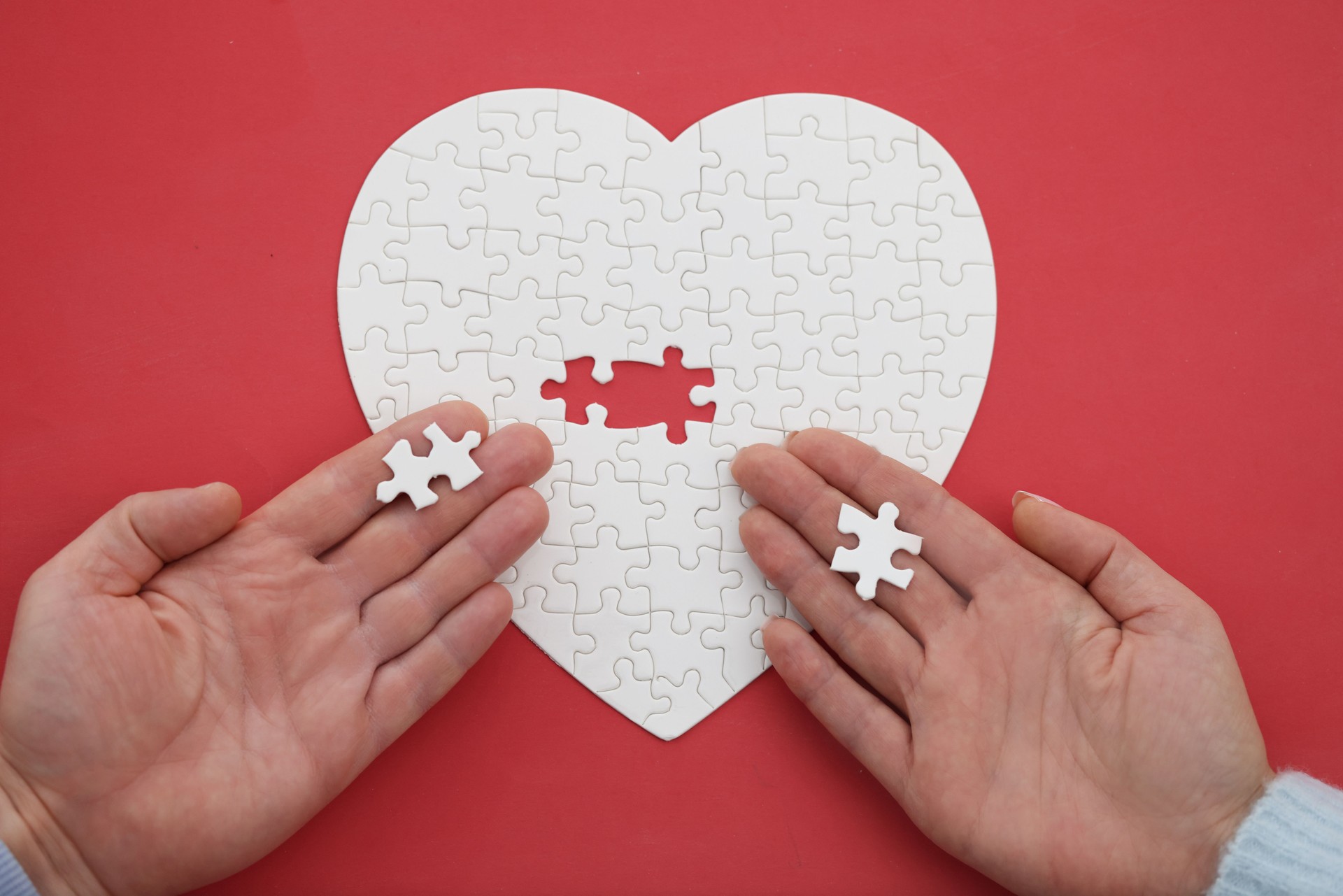 Woman and a man hand assemble jigsaw puzzle in shape of heart